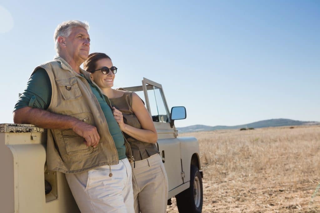 Mature couple standing by a vehicle in the veld whilst on a top safari tour for couples