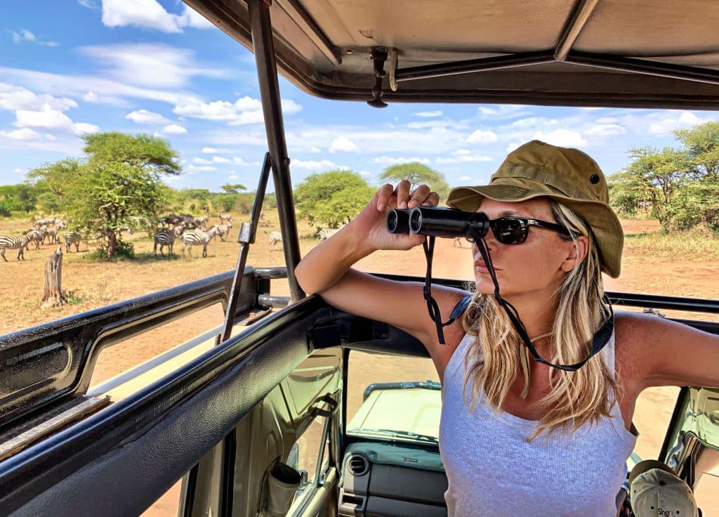 A woman with binoculars on a game drive after paying the South African safari cost