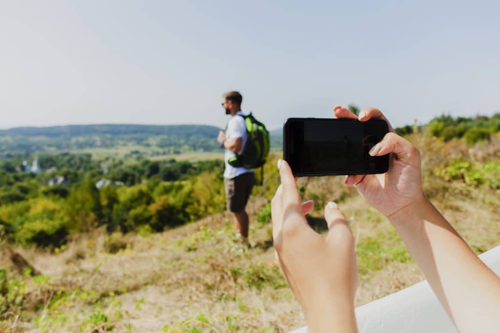 A woman taking a photo of her boyfriend in Kruger with her smartphone.