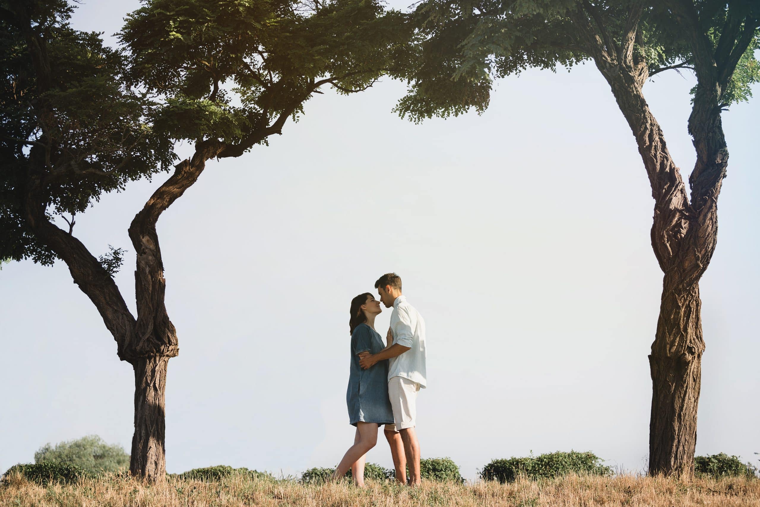 A couple embracing under two trees, capturing the essence of romance in the wild amidst a serene natural setting.