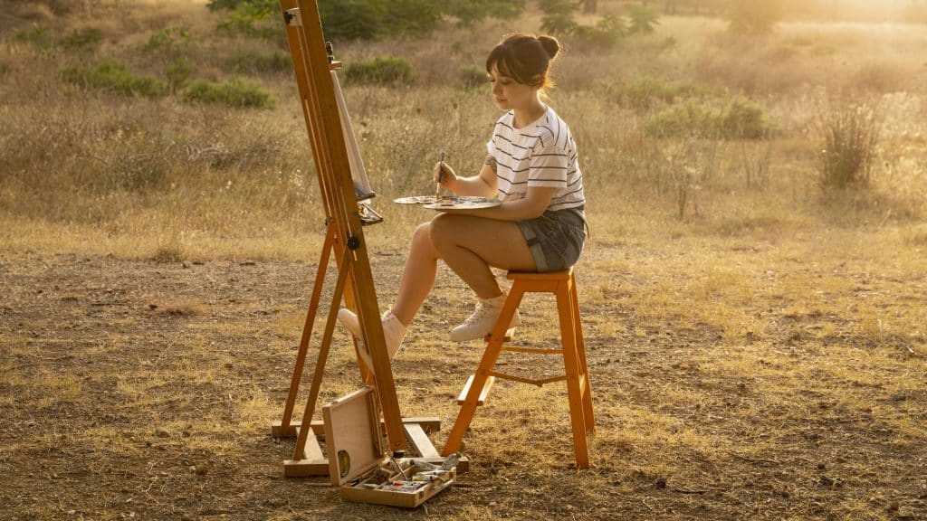A young lady sitting on a chair, painting in nature to capture safari art & inspiration